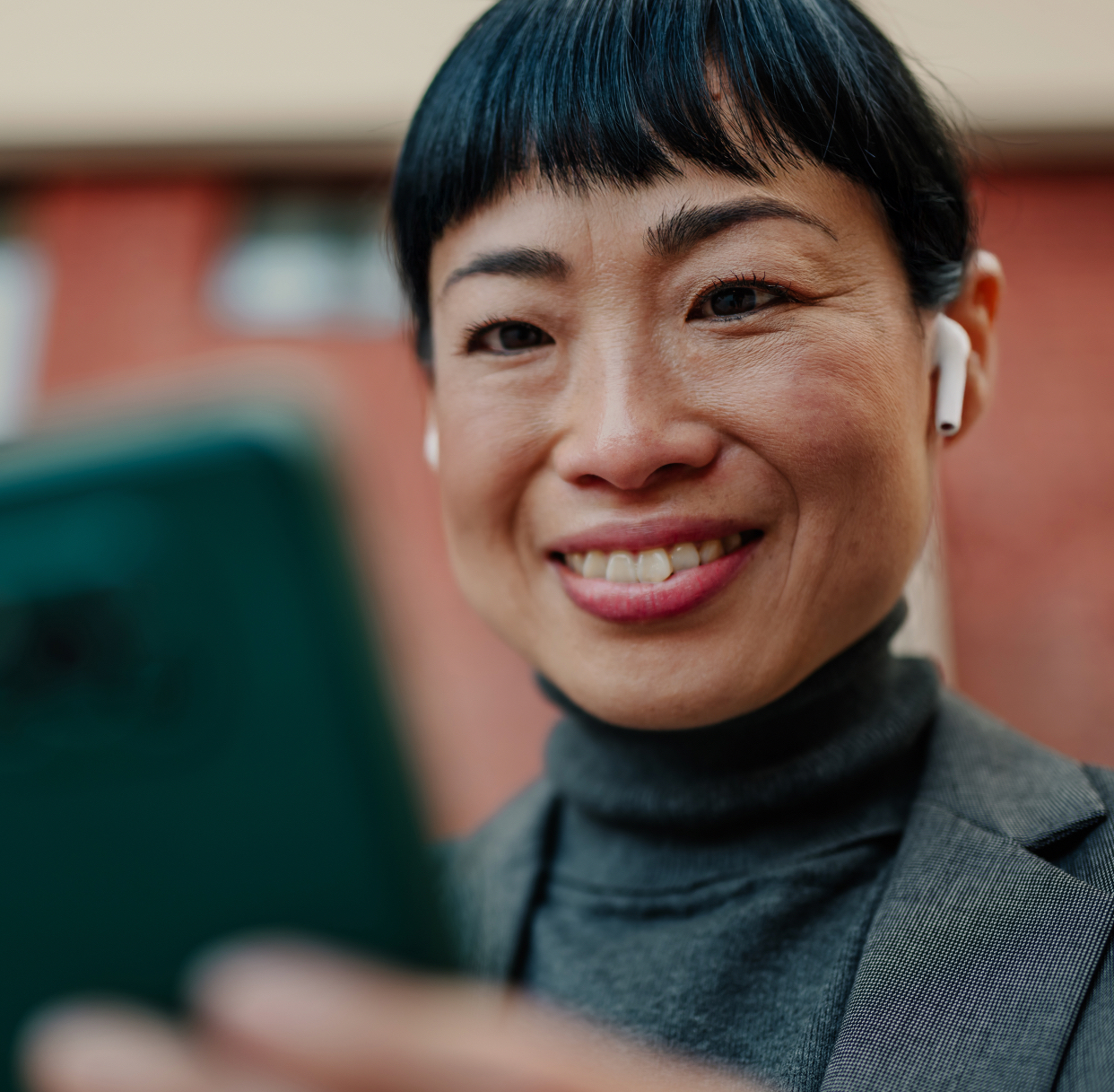 Woman smiling while wearing wireless earbuds and holding a phone